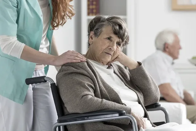 Senhora idosa sentada, acompanhada por uma profissional de saúde